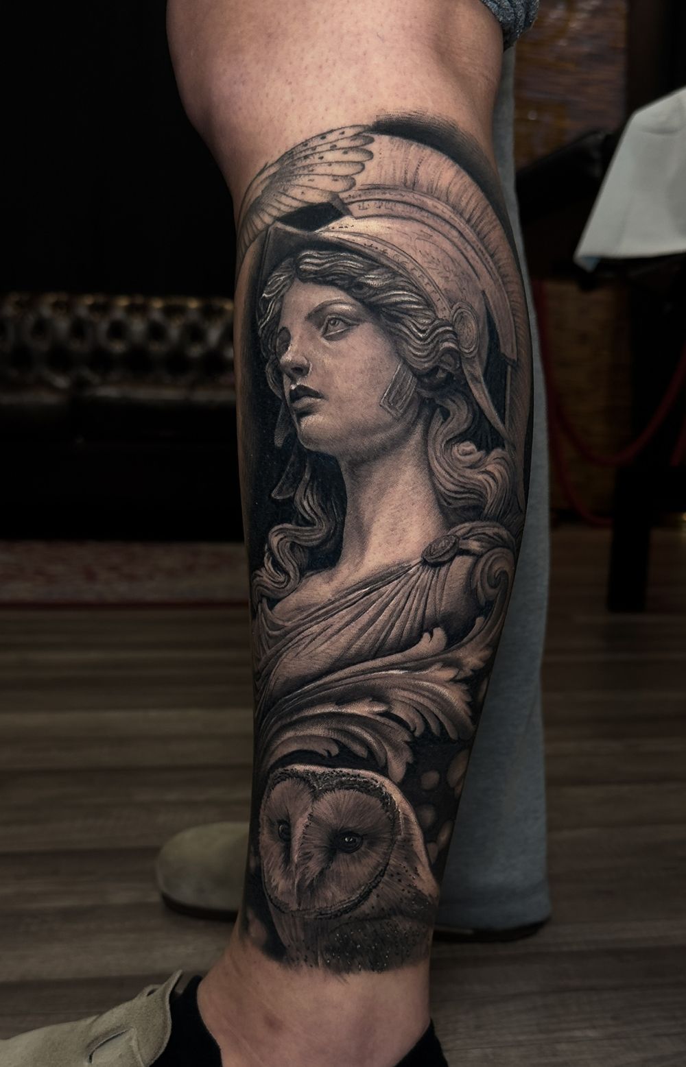 Realistic tattoo of a woman with a helmet, an owl, and ornate details on a leg.