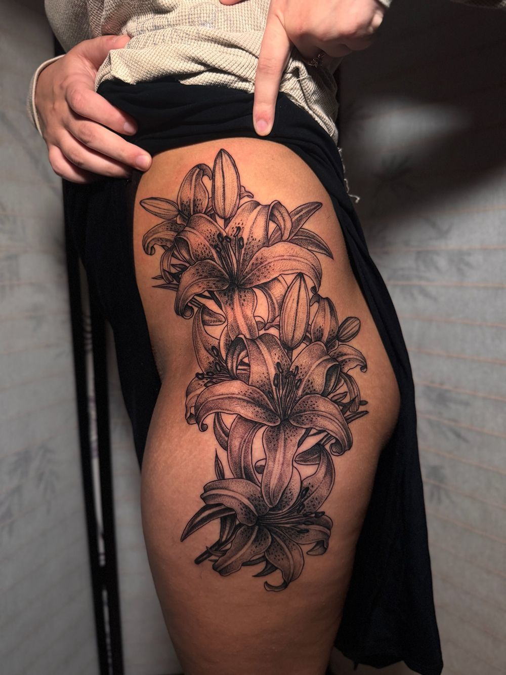 Black ink lily tattoo on a person's thigh.
