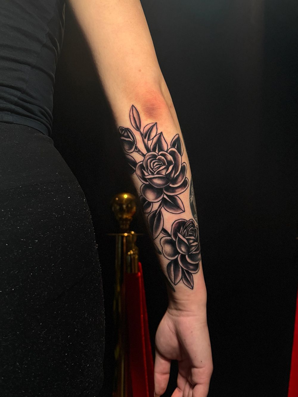 Black and white rose tattoo on a person's forearm; against a black background.