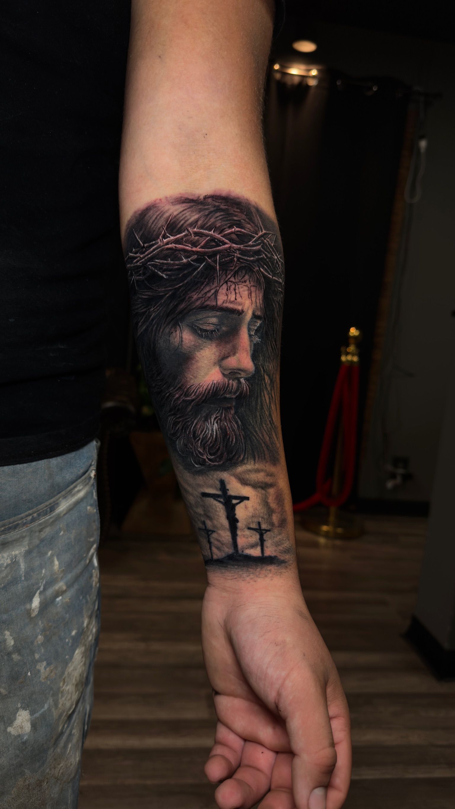 Tattoo of Jesus wearing a crown of thorns, with three crosses below. Black and gray shading.