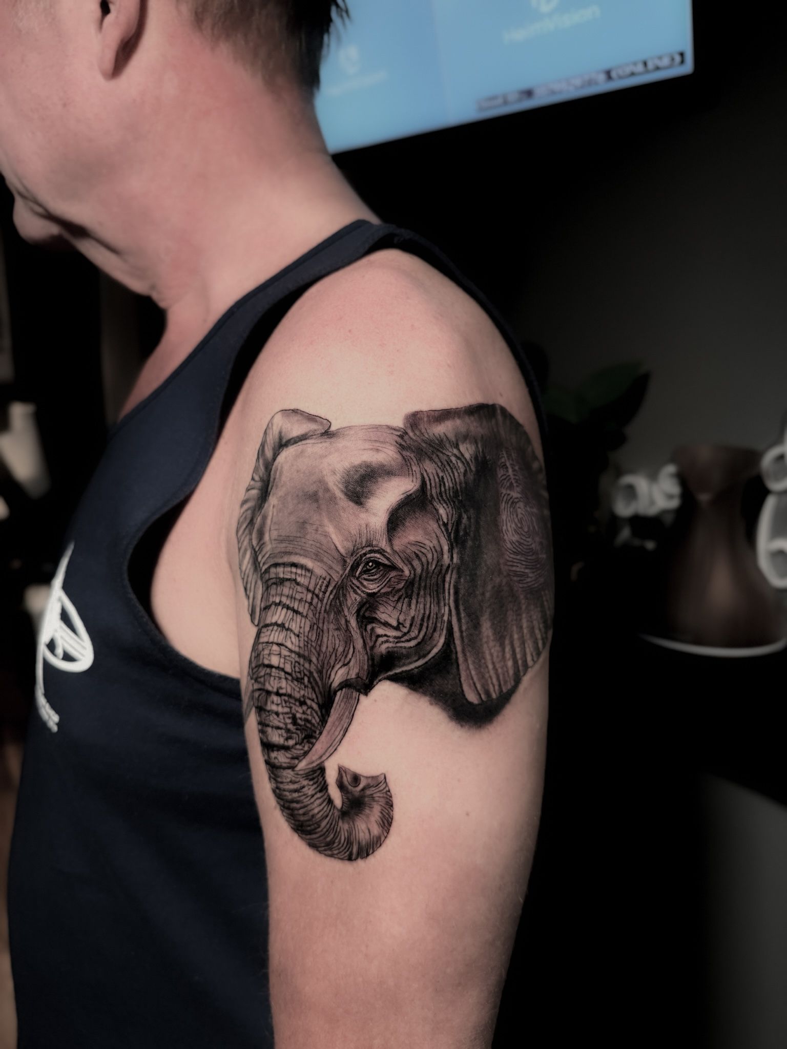 Tattoo of an elephant head on a person's upper arm. Black and gray shading with detailed skin texture.
