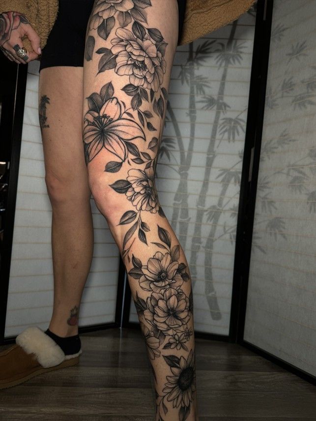 Leg with black floral tattoo, knee and thigh detail. Person in shorts and slipper.
