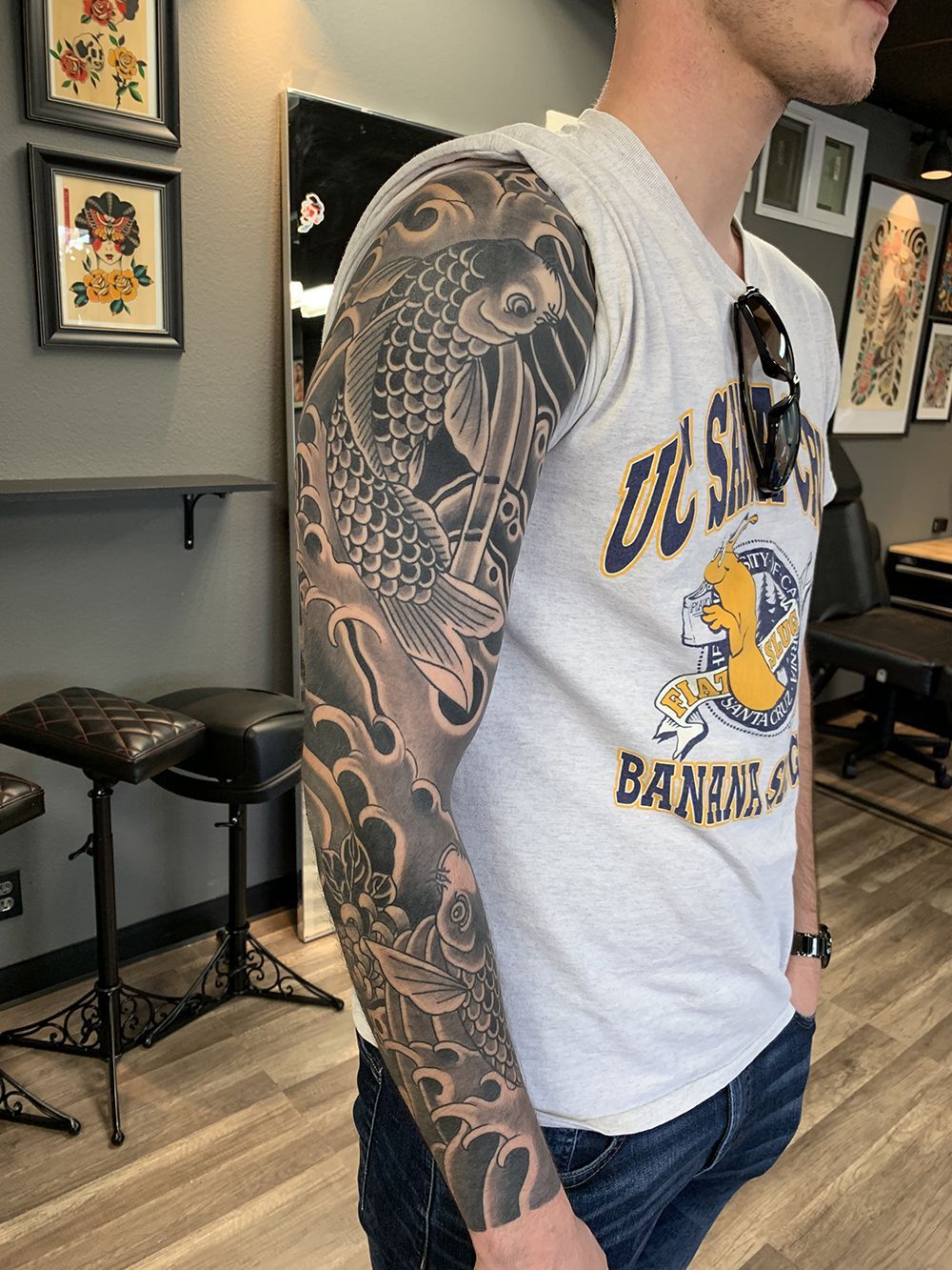 Man with a koi fish tattoo sleeve. Gray and black design; waves and ornate details. Wearing a gray t-shirt.