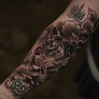 Tattoo on arm, black and grey panther's head with floral design and a landscape.