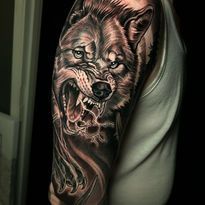 Tattoo of a snarling wolf on a person's upper arm, with detailed shading and open mouth showing teeth.