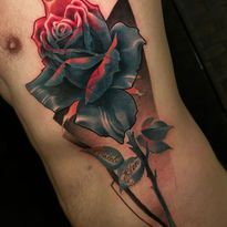 Tattoo of a blue rose with red highlights on torso, black triangle background. Stem with leaves below.