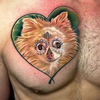 Tattoo of a Pomeranian with sugar skull makeup inside a green heart on a person's chest.