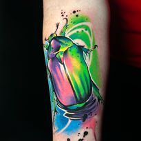 Colorful tattoo of a scarab beetle with green, purple, and pink hues on a forearm.