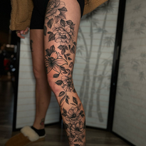 Leg tattoo of blooming flowers and leaves on a person's leg.