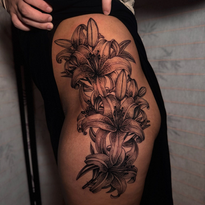 Black and white lily tattoo on a person's thigh.