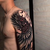 Man's arm and shoulder tattoo featuring a black raven with detailed wings and a reddish chest.