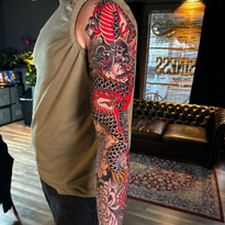 Man with full sleeve tattoo of a red and black dragon in tattoo studio.