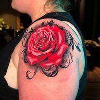 A vibrant red rose tattoo with black swirls on a person's shoulder.