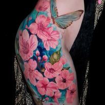 Colorful tattoo of pink flowers and a butterfly on a person's thigh, with teal and blue background.