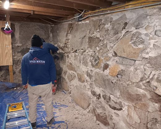 Person in a blue jacket working in a stone basement wall under renovation.