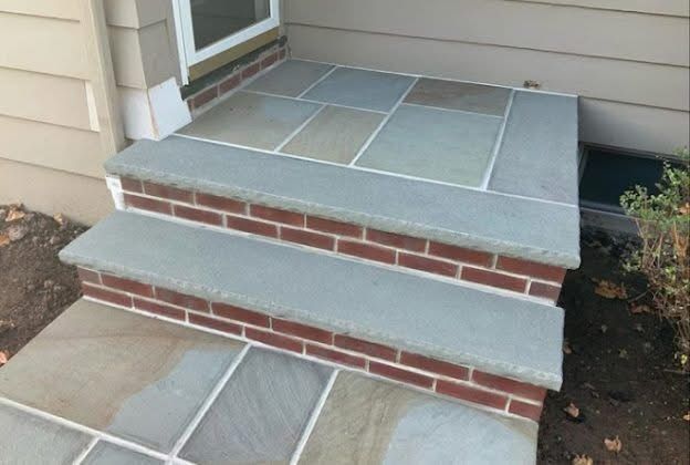 Front porch steps with gray stone treads and red brick risers leading to a house entrance