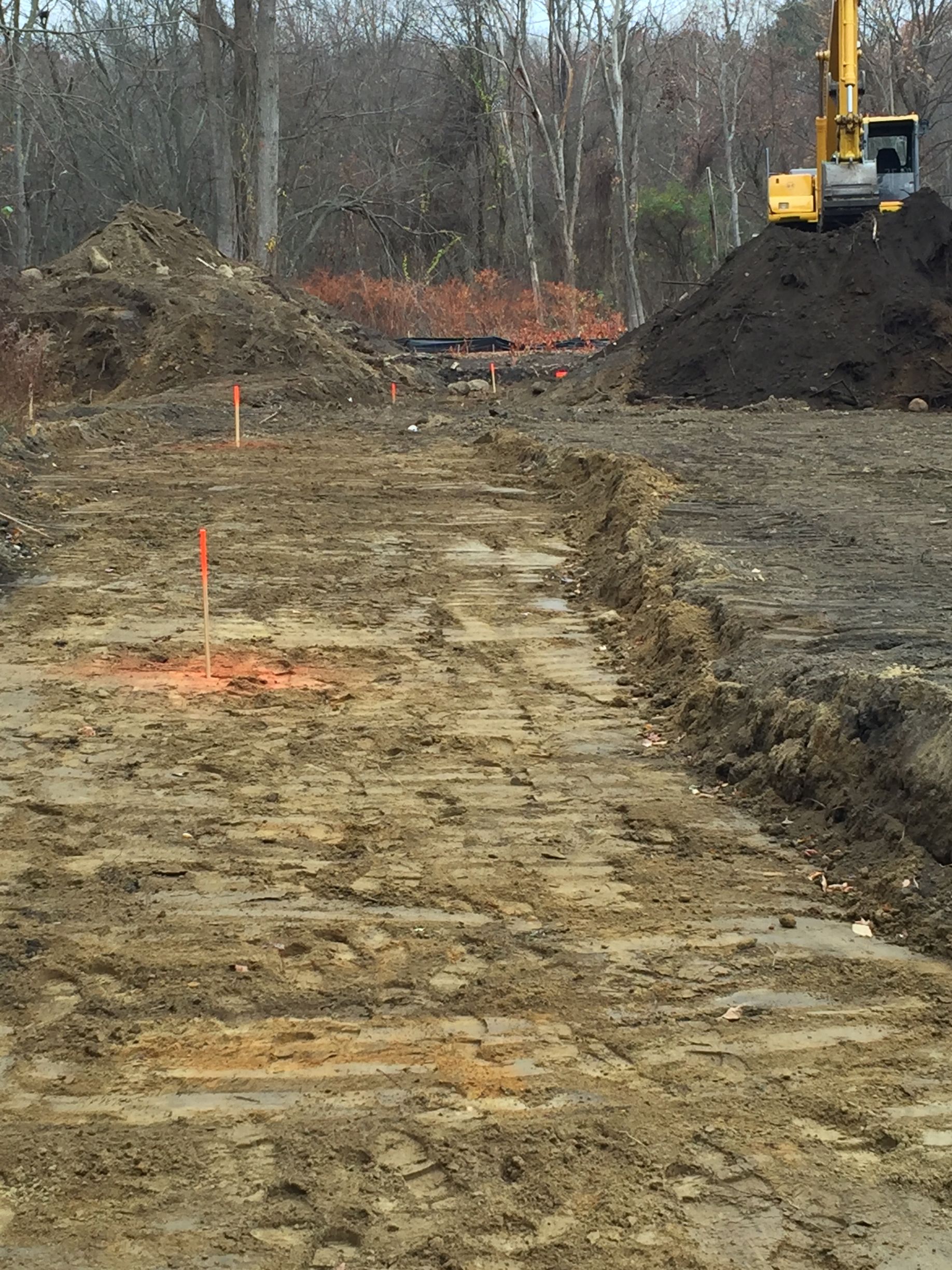 Construction site with graded dirt road, orange markers, and an excavator beside a soil pile