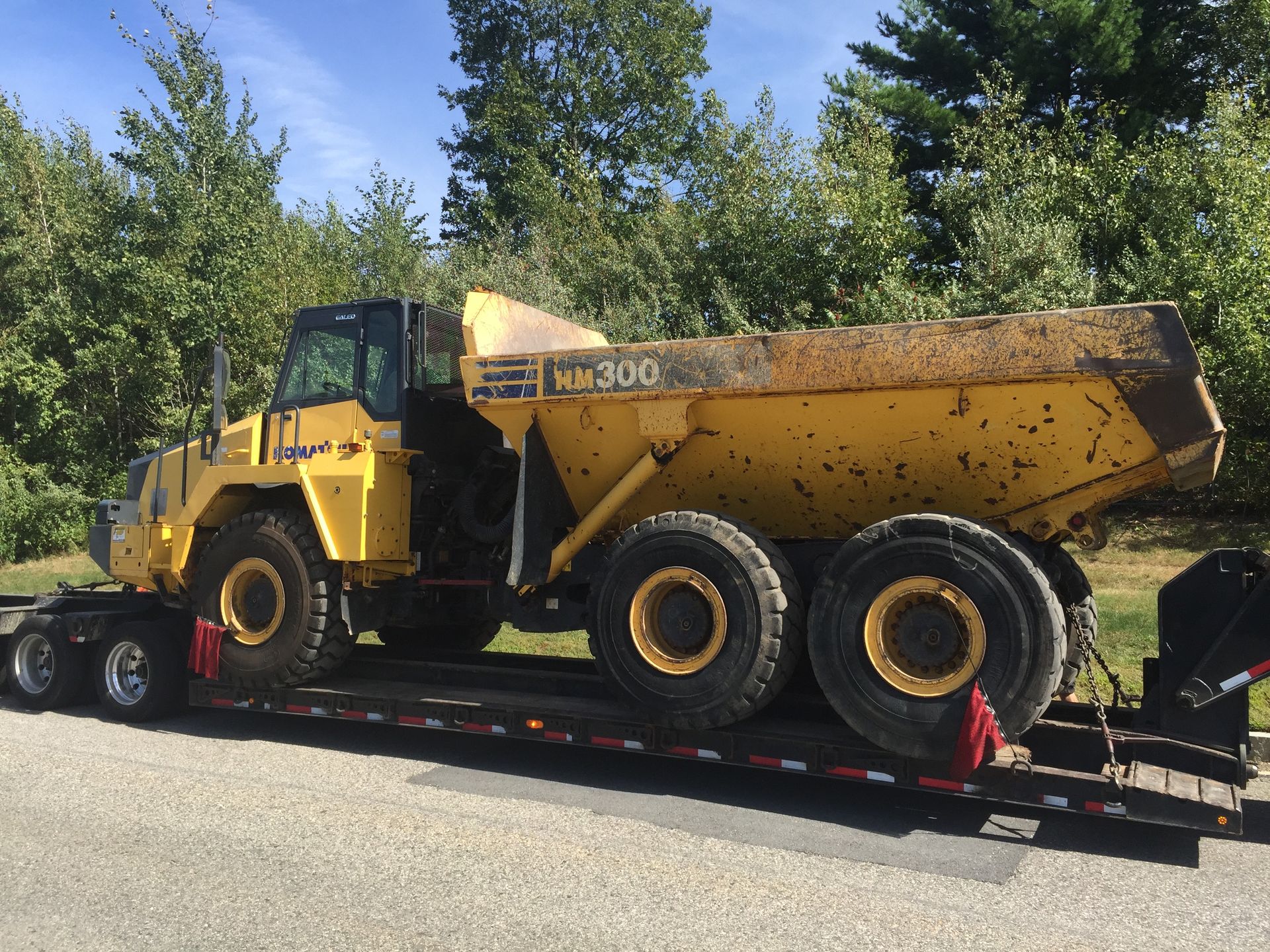 Yellow road grader on a flatbed trailer in a wooded area