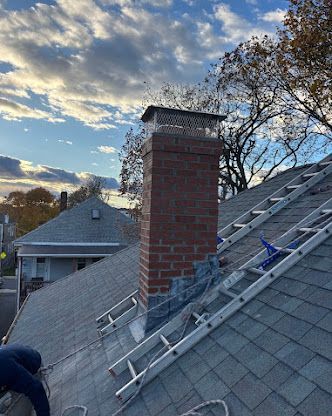 Roof repair with ladders beside a brick chimney at sunset