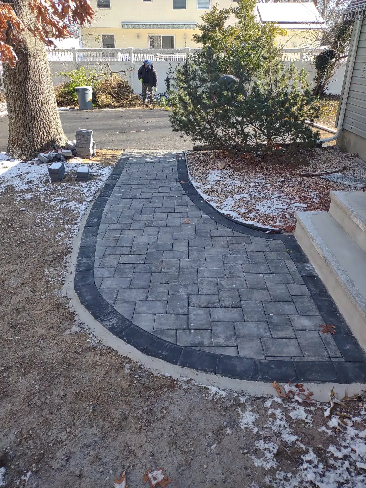 Curved stone walkway through a snowy garden, leading toward a person near a building entrance