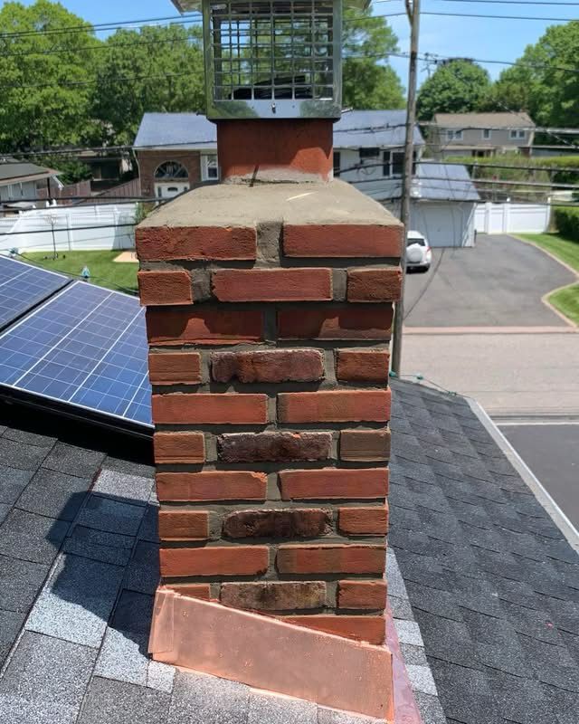 Brick chimney on a shingled roof beside solar panels, viewed from above with a street and houses in the background
