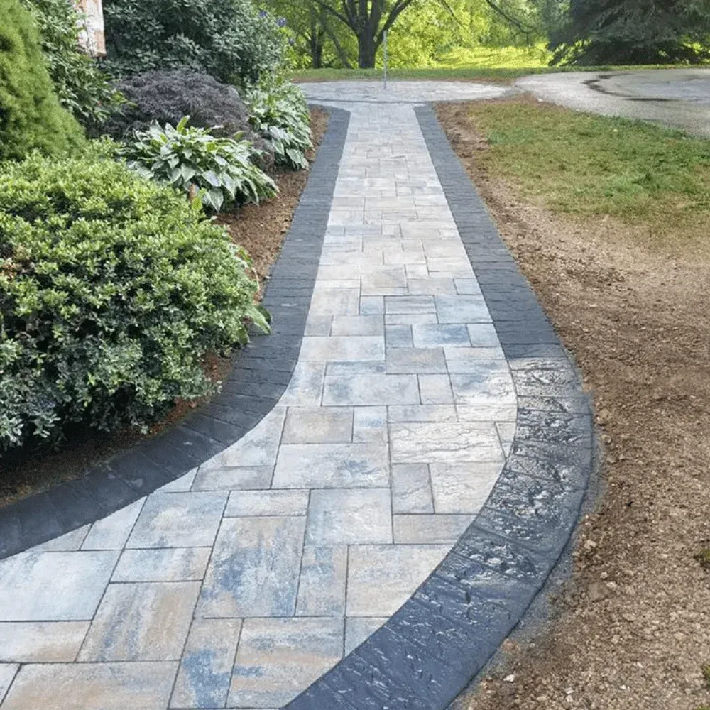 Curved stone walkway bordered by dark edging, shrubs, and grass in a landscaped garden.