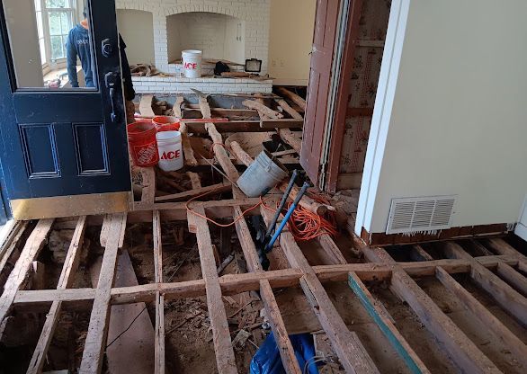 Wood floor under renovation with exposed joists and scattered tools in a house interior