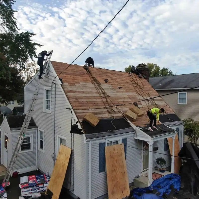 Workers repairing a storm-damaged house roof with tarps, boards, and ladders