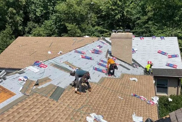 Roofers installing new shingles on a house roof, with underlayment exposed and trees in the background