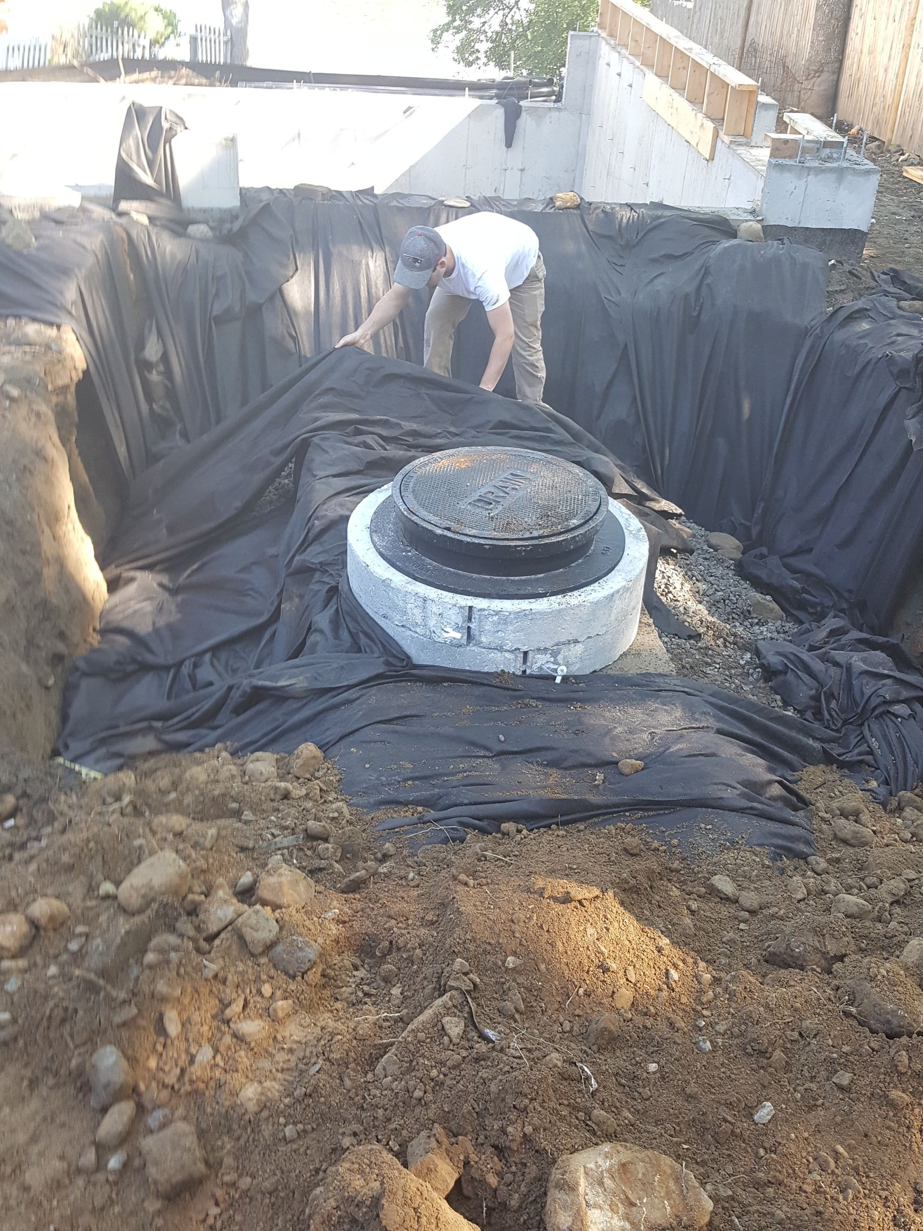 Worker lining a black waterproof pit around a circular concrete structure at a construction site