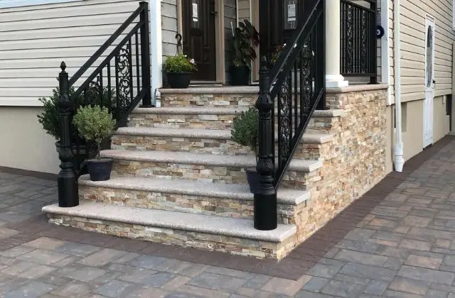 Front steps of a house with stone siding, black railings, and a paved walkway