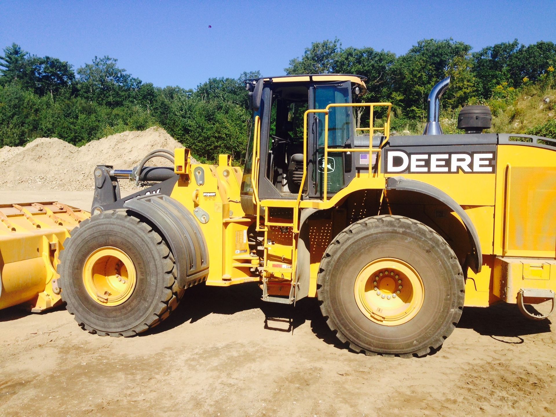Yellow John Deere wheel loader parked on a dirt lot with sand piles and trees in the background