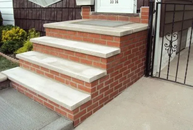 Brick front steps with white concrete treads leading to a house entrance.