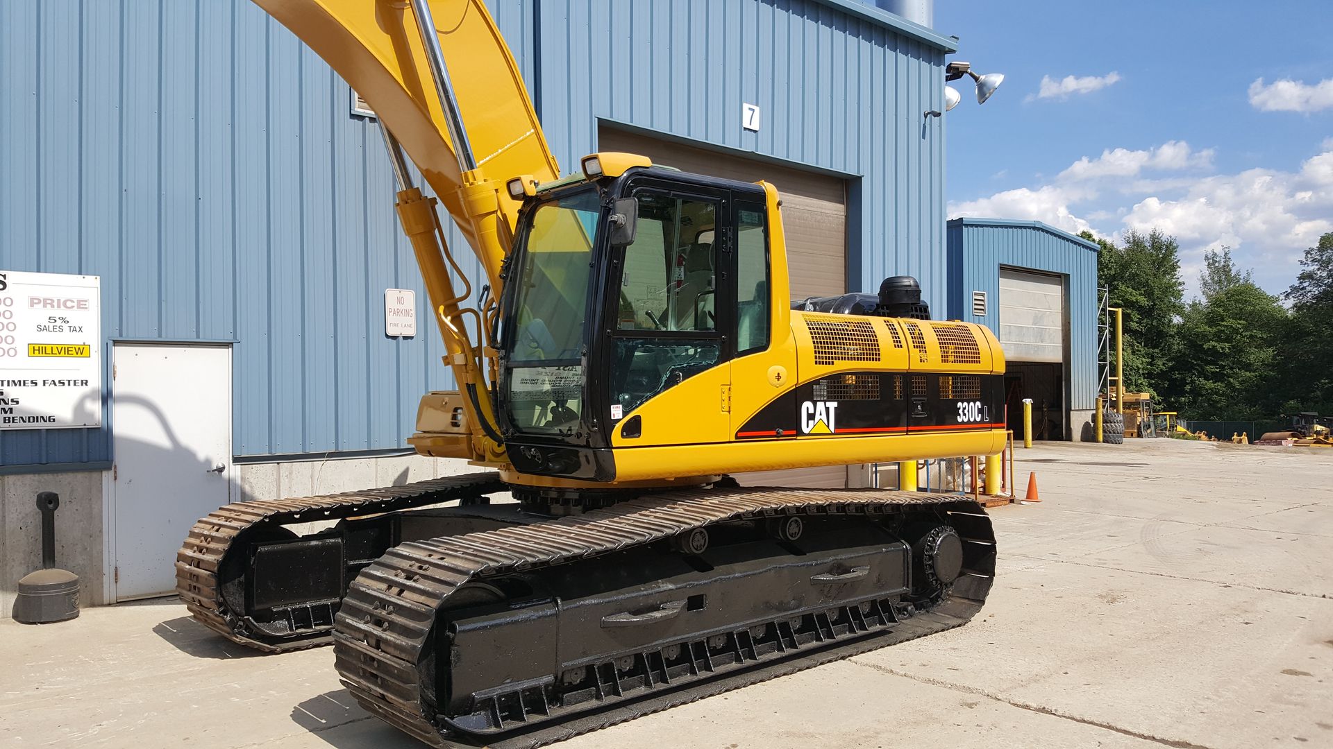 Yellow excavator on tracks parked beside a blue industrial building.