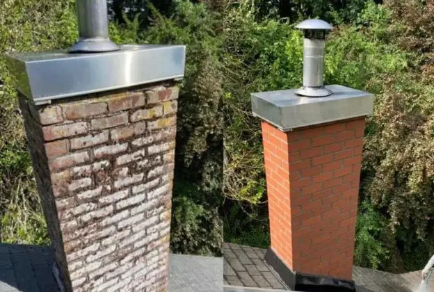 Two brick chimneys with metal caps and flues on a rooftop, one weathered and one red-orange.