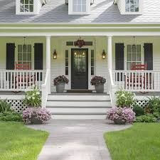 Front porch of a white house with green shutters, black door, and flower pots along the steps