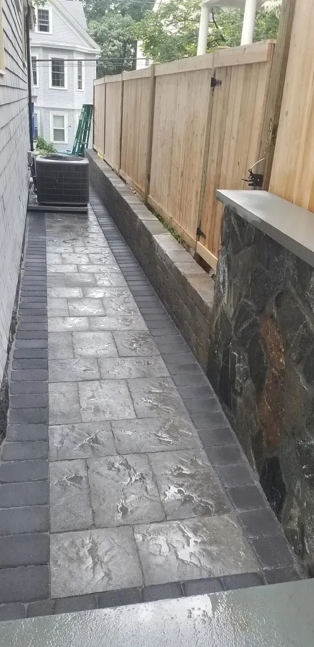 Narrow wet stone walkway beside a wooden fence, leading between houses.