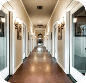 Long hallway with doors on both sides, sconce lights, and reflective dark flooring.