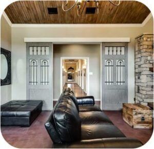 Living room with black leather couch, gray sliding doors, and a long hallway in the background.