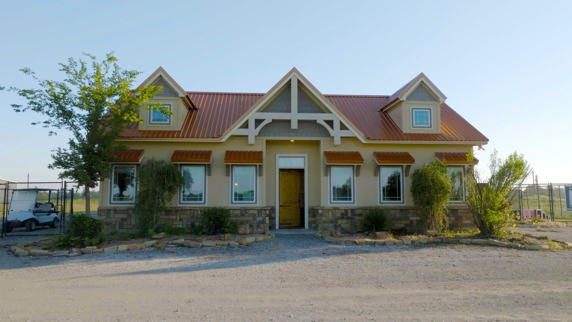 Tan building with a red tile roof and stone accents; windows with beige trim; clear blue sky.