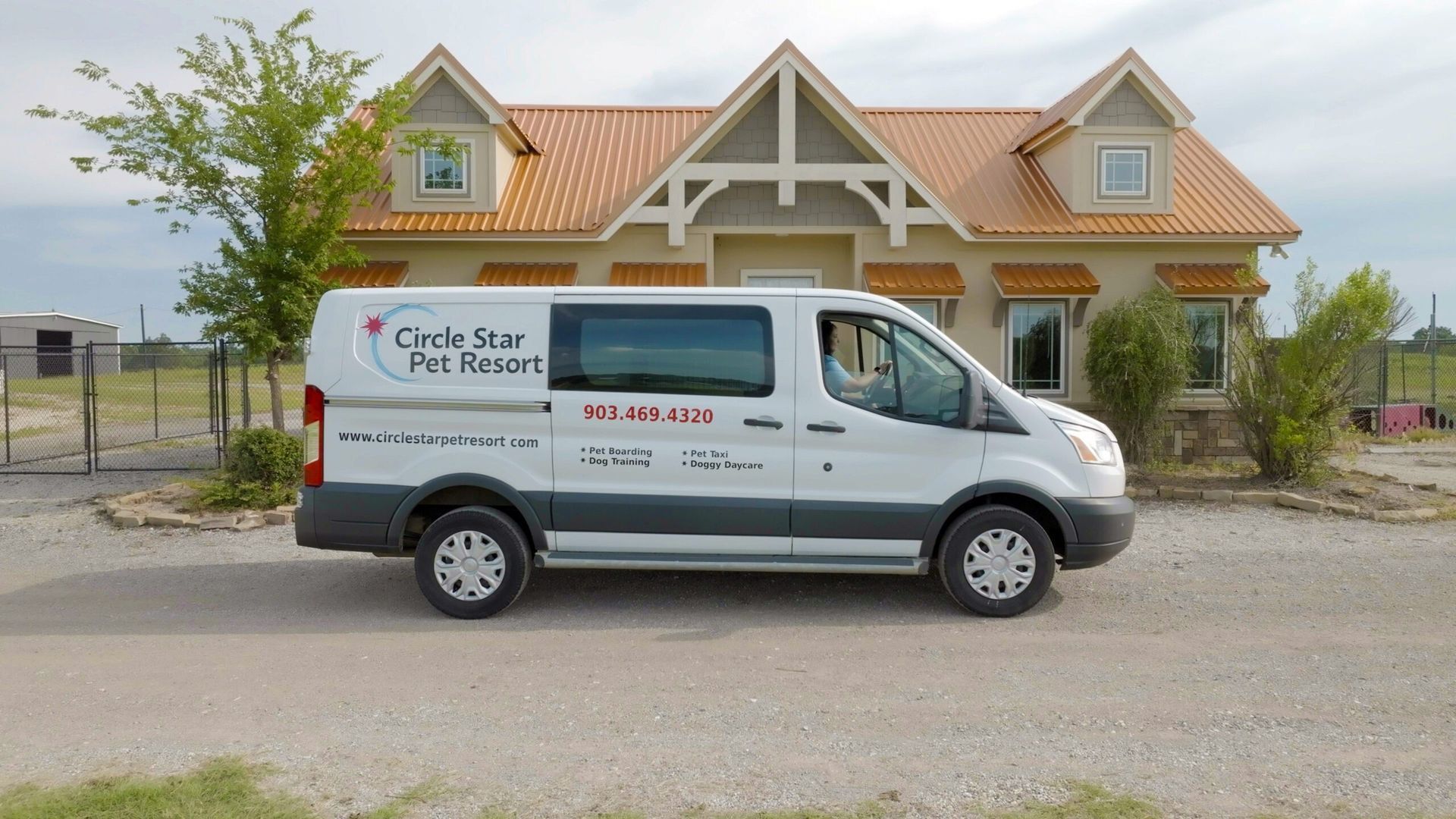 White van with "Circle Star Pet Resort" parked on dirt road in front of a tan house with orange roof.