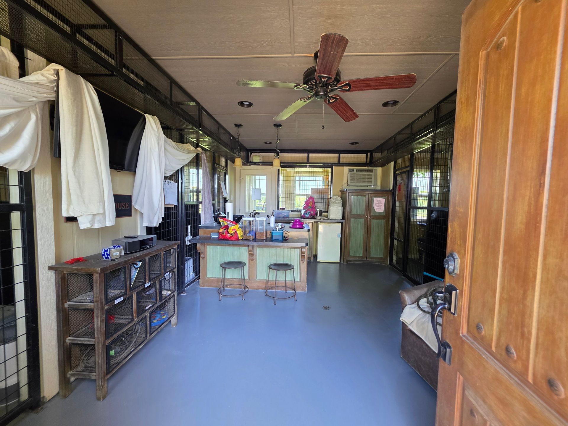 Interior of a room with open door, a kitchen island, and a ceiling fan. Clothes hang on the left side.