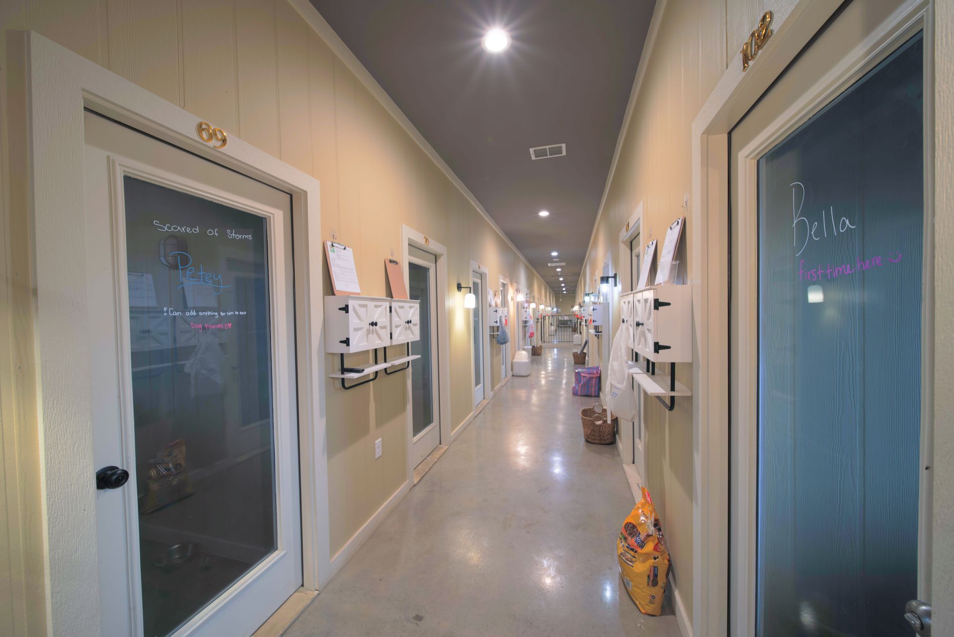 Long hallway with doors and white mailboxes. Bright lighting with beige and grey colors.