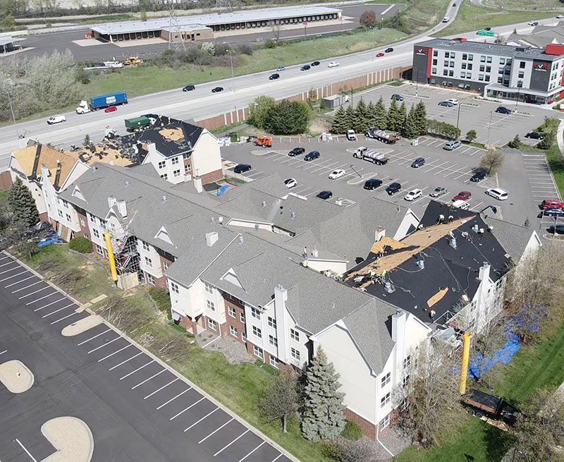 Aerial view of a damaged apartment complex with missing roofs and cars in a parking lot.