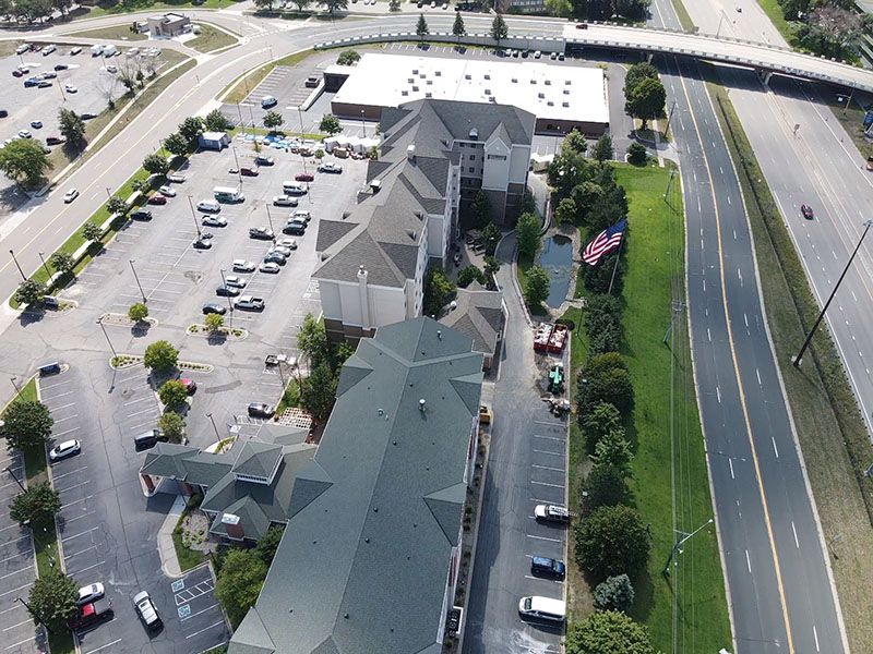Aerial view of a hotel next to a highway, with parking lot and trees surrounding it.