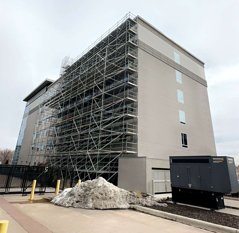 Gray building with scaffolding, snow pile, and a generator.