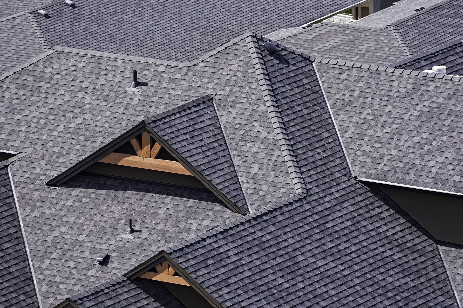 Close-up of a complex gray asphalt shingle roof with wooden gable accents and vents.