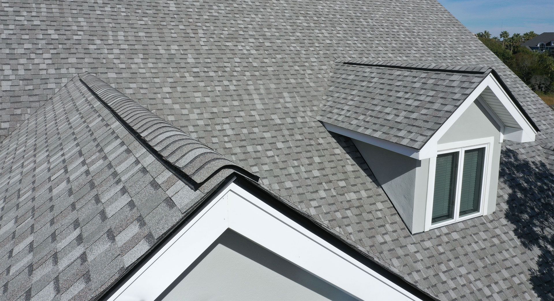 Gray shingled roof with a dormer, against a clear sky.