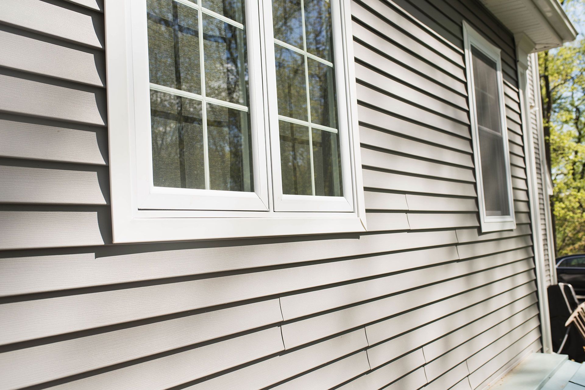 Gray siding on a house with white-framed windows, against a backdrop of trees.