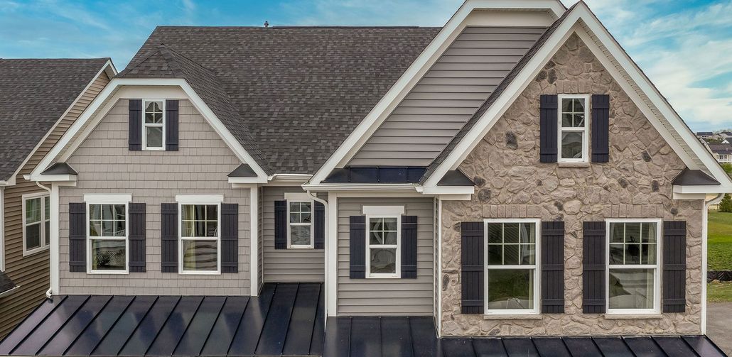 Exterior of a house with various siding and a dark roof. Windows have black shutters.